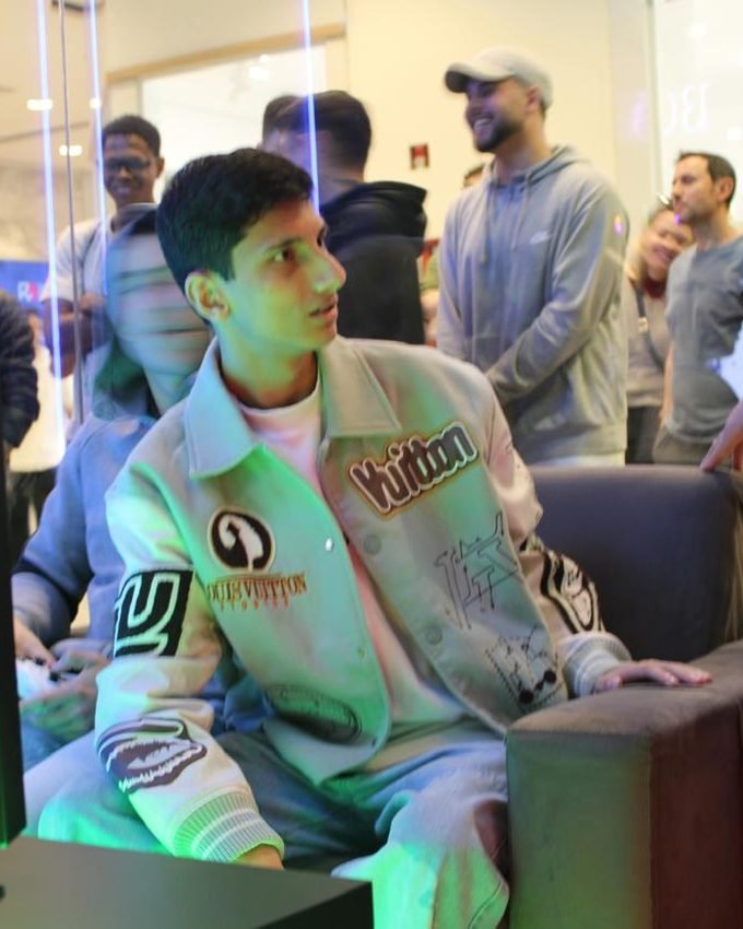 Paivinha jogando num evento, com o controle na mão e o público em volta.